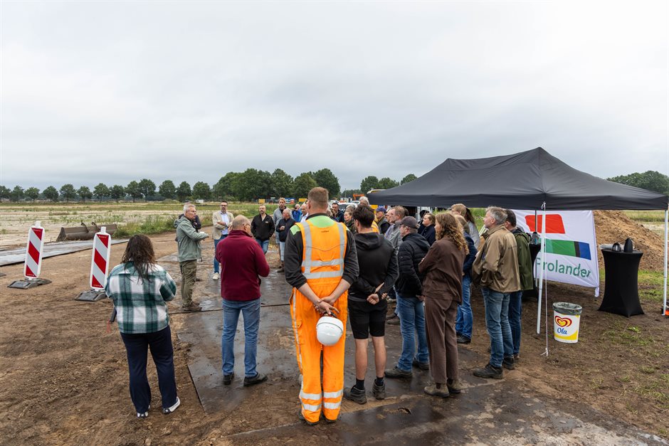 Een grote groep mensen luistert buiten naar een toelichting, bij een tent met een Prolander-vlag